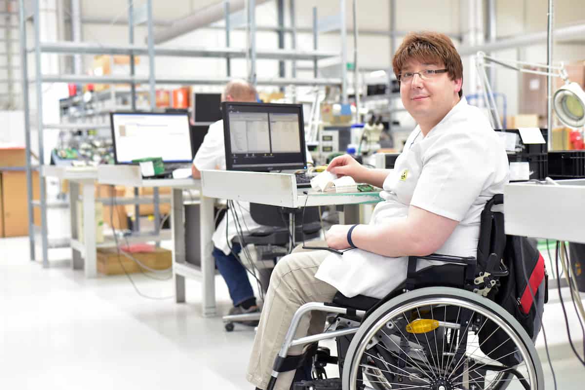 Rollstuhlfahrer am Arbeitsplatz in einer Fabrik zur Montage von Elektronik – Alltag mit Gehbehinderung // Wheelchair driver at the workplace in the industry